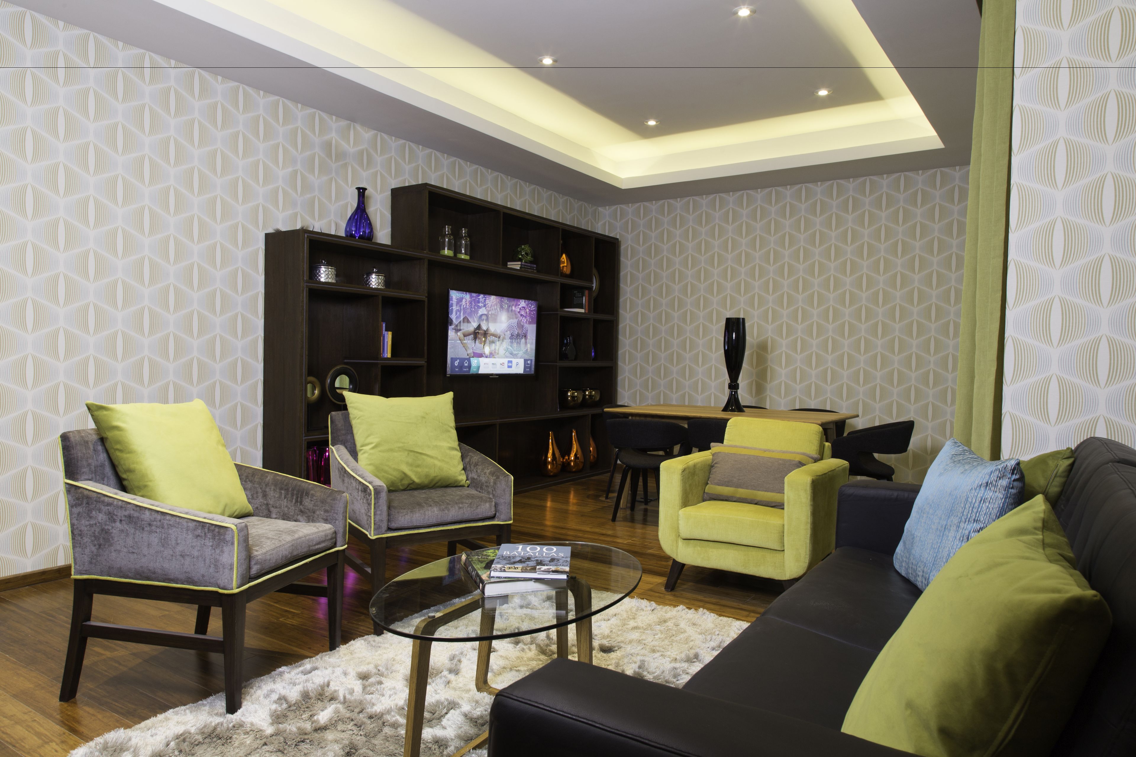 A modern living room with a sofa, armchairs, a coffee table, and a TV on a stand.
