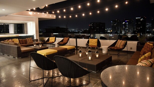 A rooftop lounge with a city view, string lights, and modern furniture. - Hotel Love It CAS Consulate (Guadalajara)