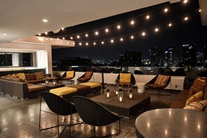 A rooftop lounge with a city view, string lights, and modern furniture.