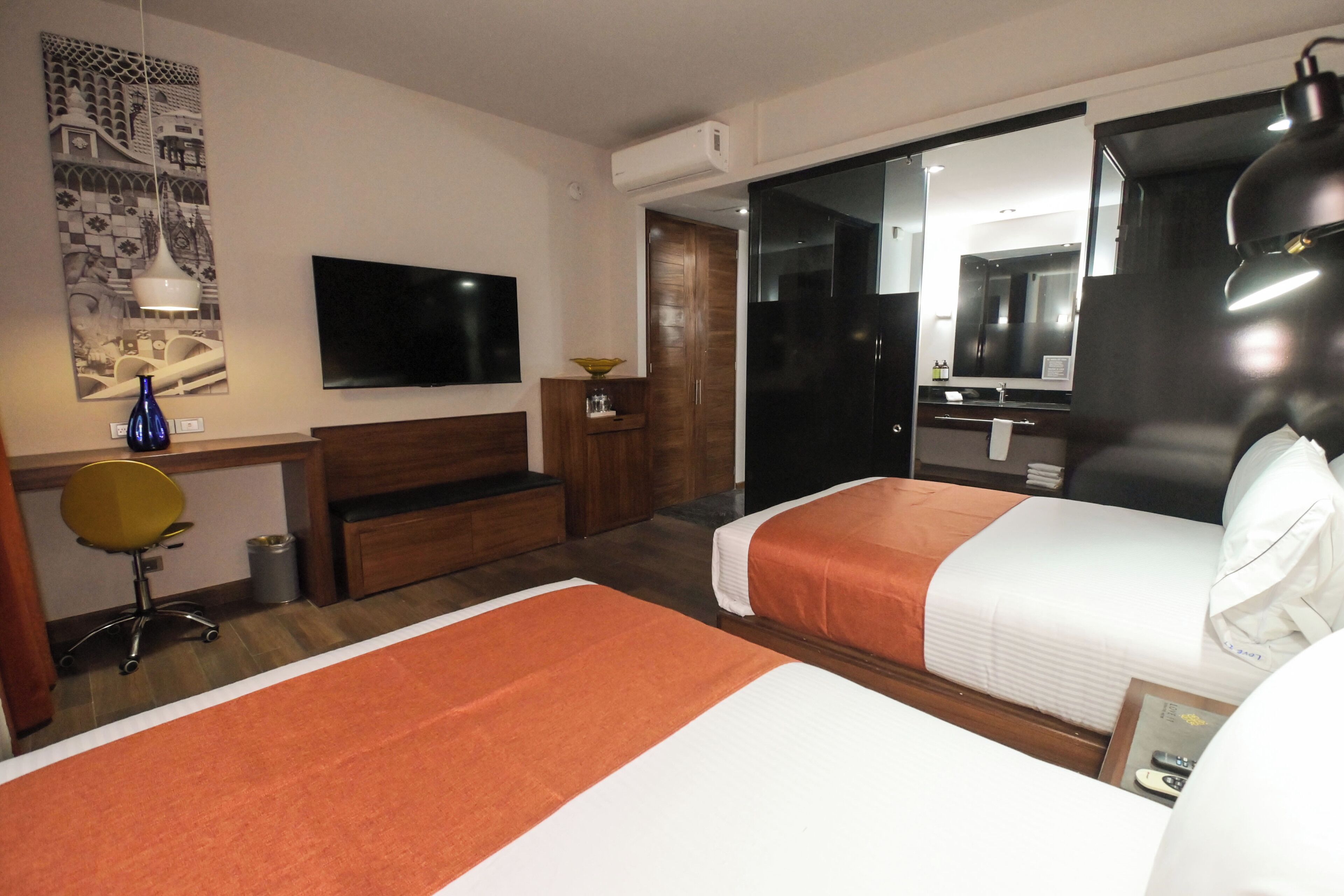Ein Hotelzimmer mit zwei Betten, einem Fernseher, einem Schreibtisch und einem Badezimmer.