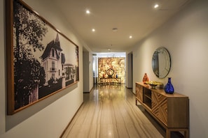 A hallway with a large framed picture on the left, a wooden console table with vases on the right, and a patterned wall in the background. - Hotel Love It - CAS Consulado (Guadalajara)