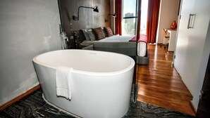A modern hotel room with a large bathtub, a bed with multiple pillows, a desk, and a chair. - Hotel Love It CAS Consulate (Guadalajara)