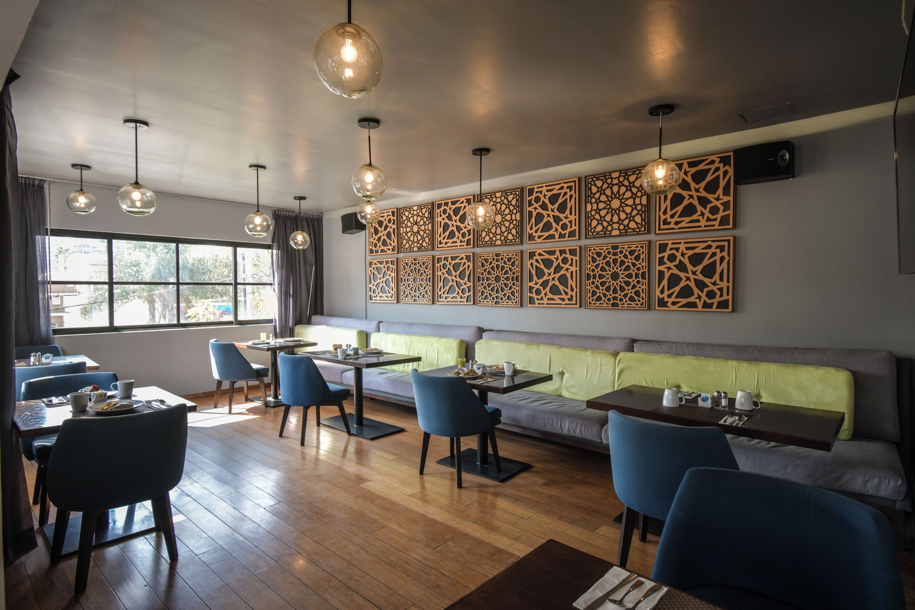 A modern dining area with wooden tables, blue chairs, and a green cushioned bench.