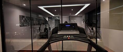 Un gimnasio moderno con cinta de correr, equipo de ejercicio y vistas a la ciudad a través de amplias ventanas.