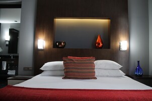 Habitación de hotel con una cama grande, una colcha roja, un cojín estampado y un florero en la mesita de noche.