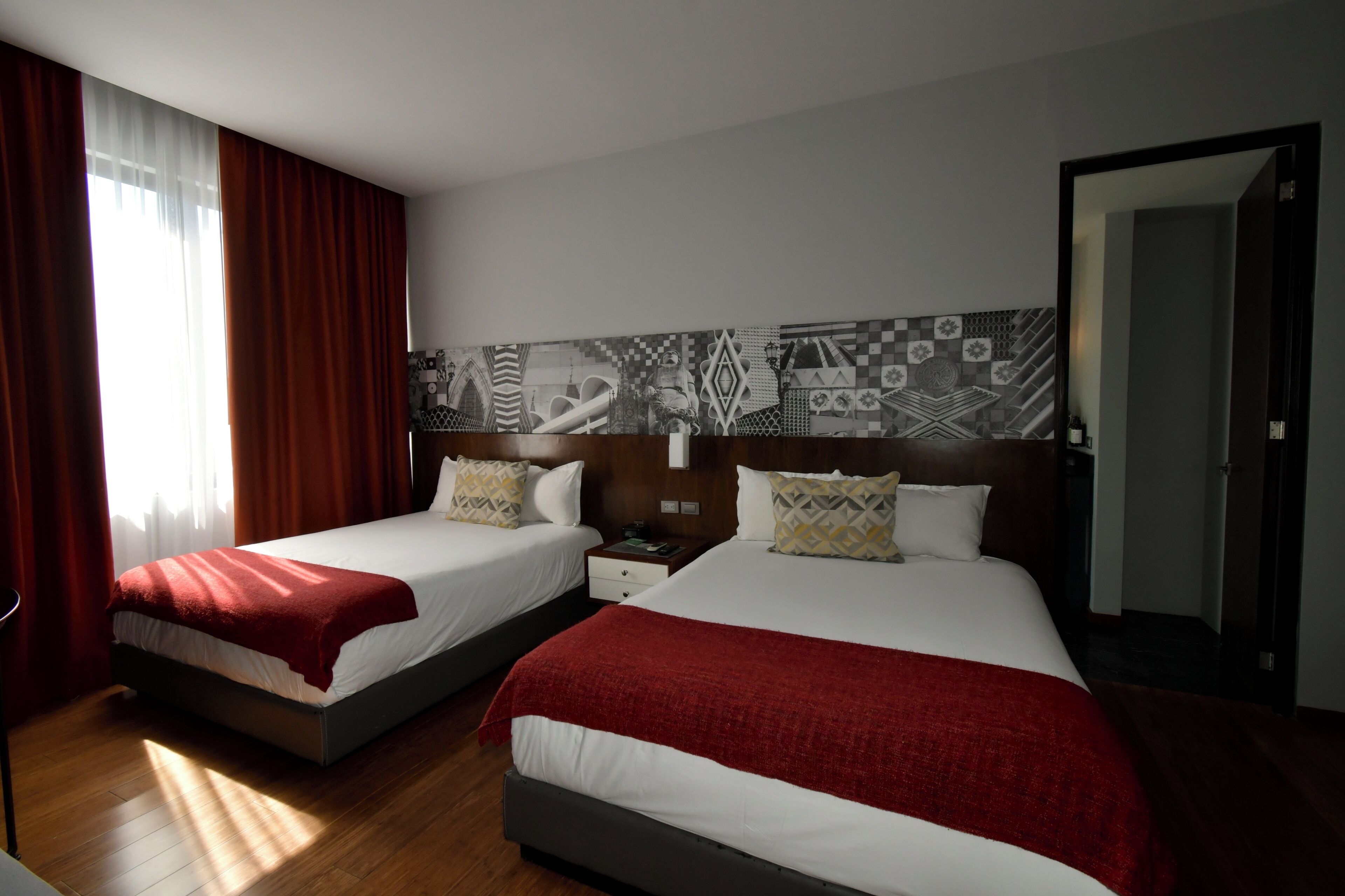 Une chambre d’hôtel avec deux lits, une table de chevet, un mur recouvert de carreaux décoratifs et une porte.