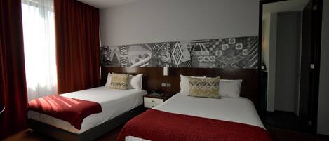 Une chambre d’hôtel avec deux lits, une table de chevet, un mur recouvert de carreaux décoratifs et une porte.