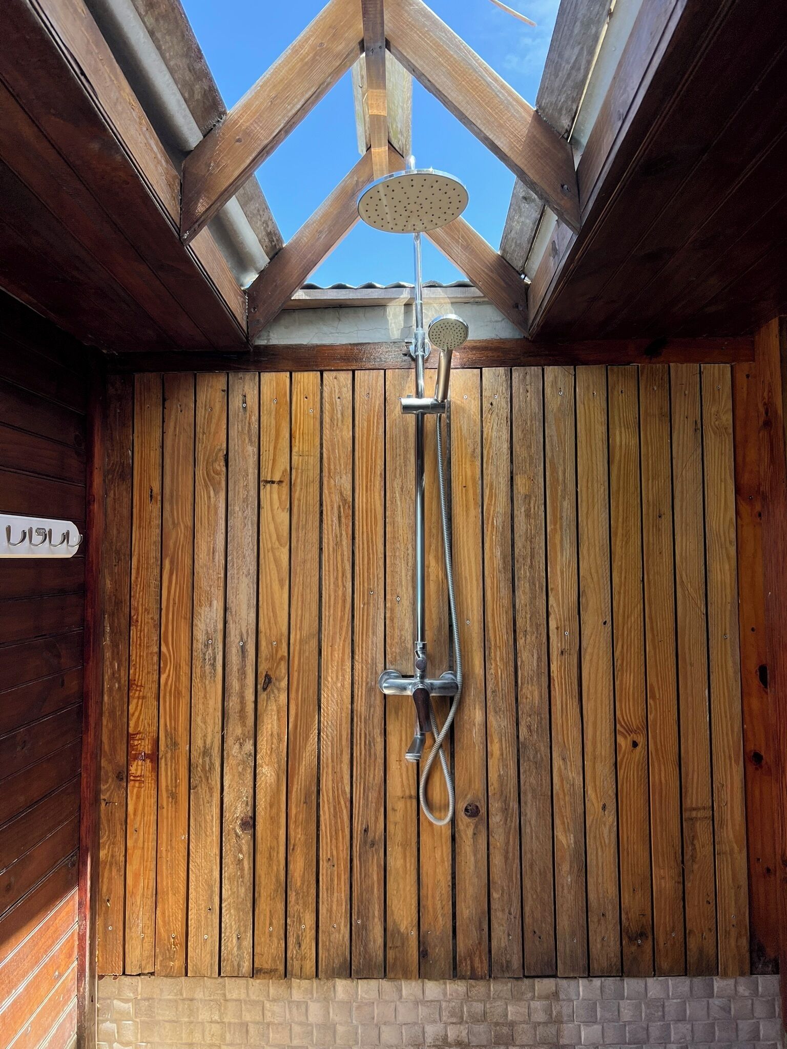 A wooden shower enclosure with a skylight, a metal showerhead, and a hose.