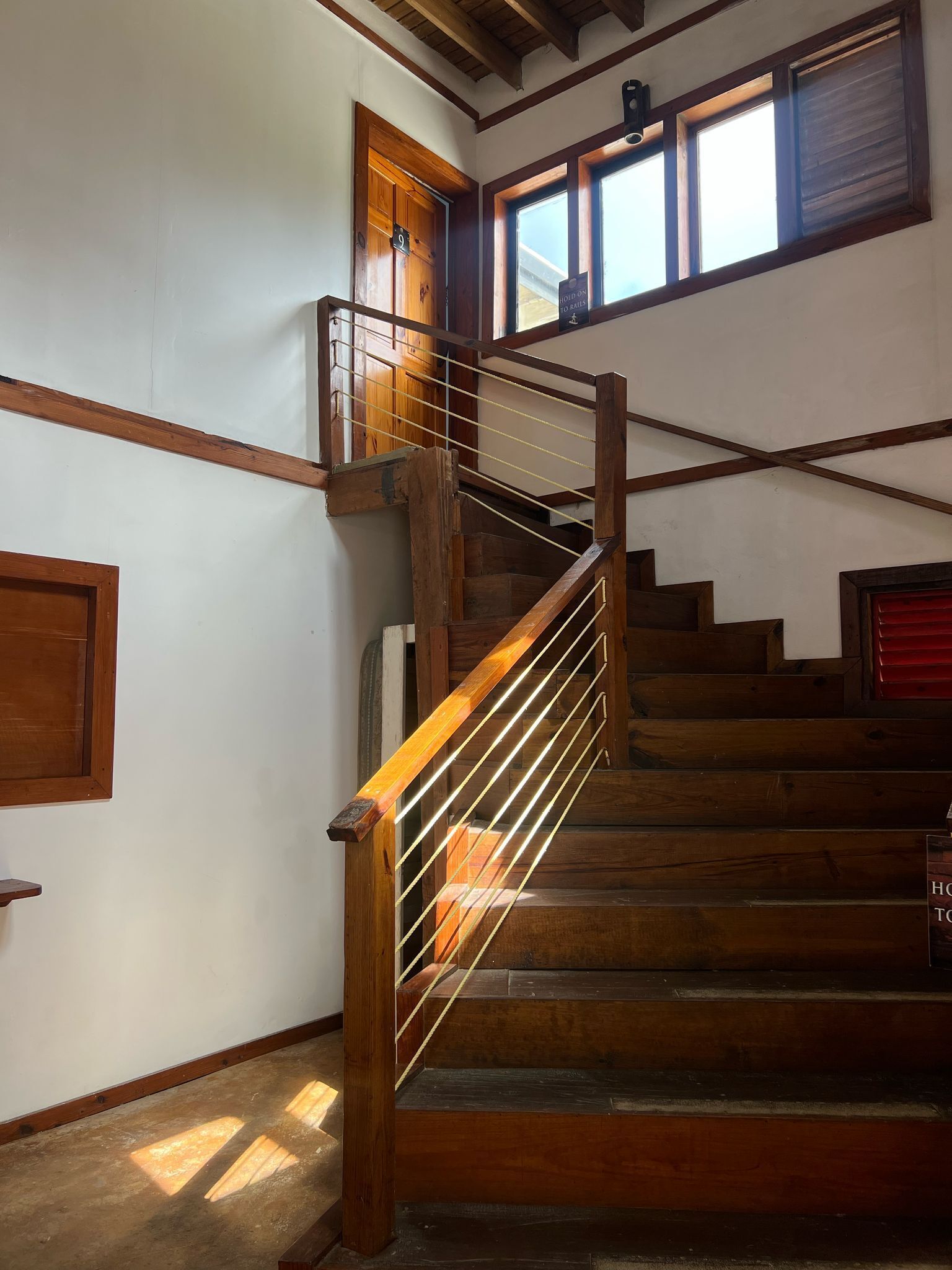 A wooden staircase with a handrail, a door with a number, and a window with a sign.