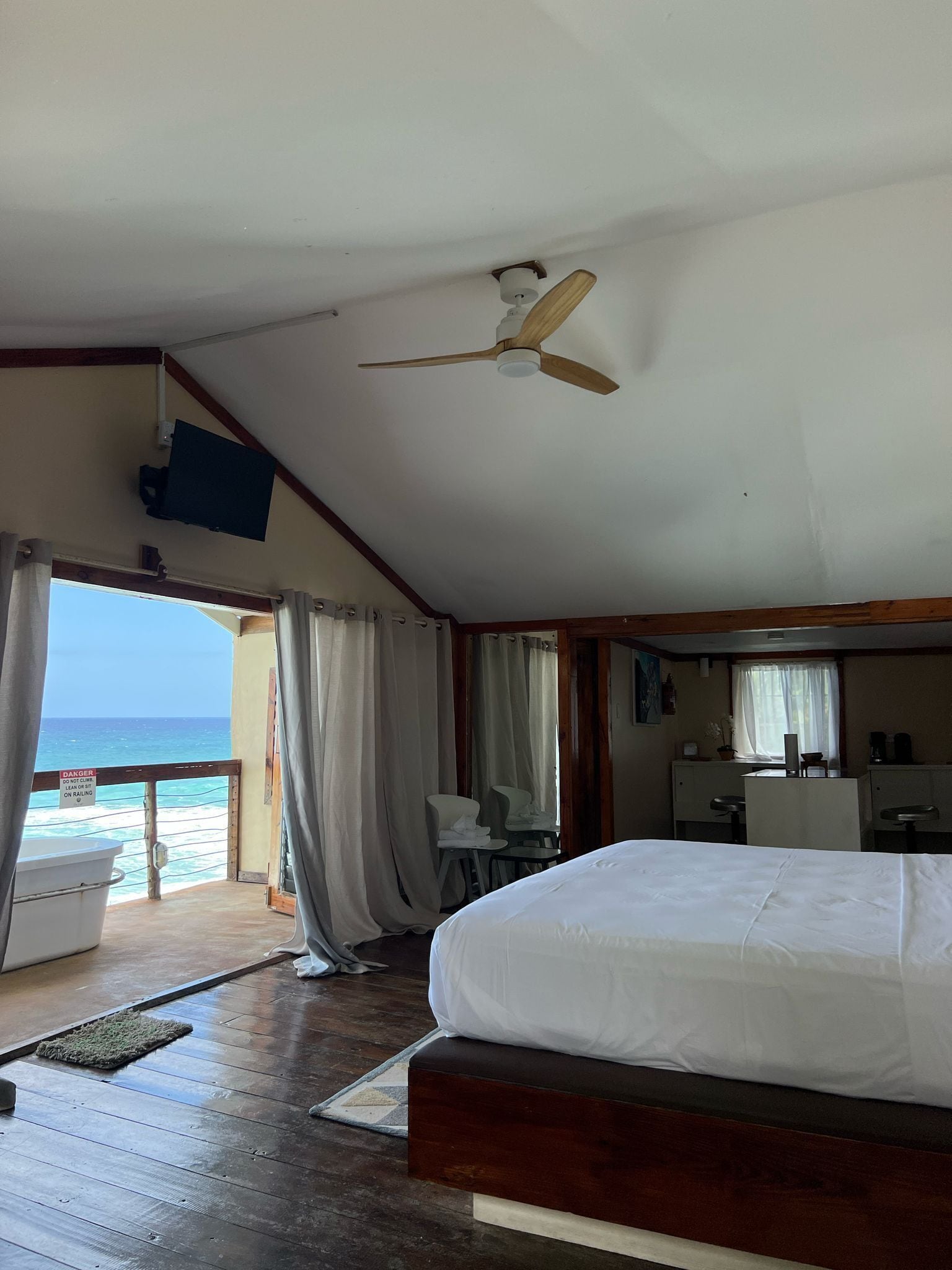 A room with a bed, a desk, a chair, a ceiling fan, and a view of the ocean.