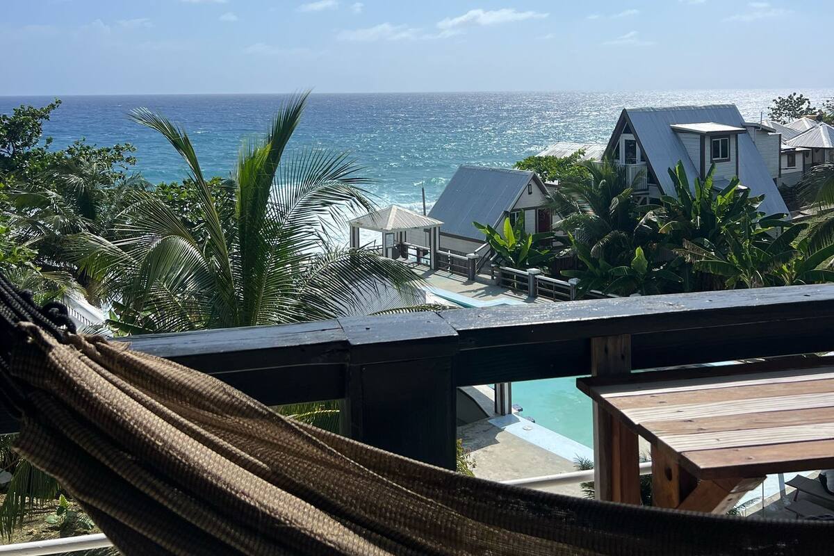 Una hamaca con vista a una playa y al océano, con una casa que tiene piscina.