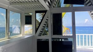Una habitación con vistas al océano, paredes blancas y un techo con vigas de madera.