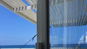 Un balcón frente a la playa con vista al océano, una hamaca y un ventanal.
