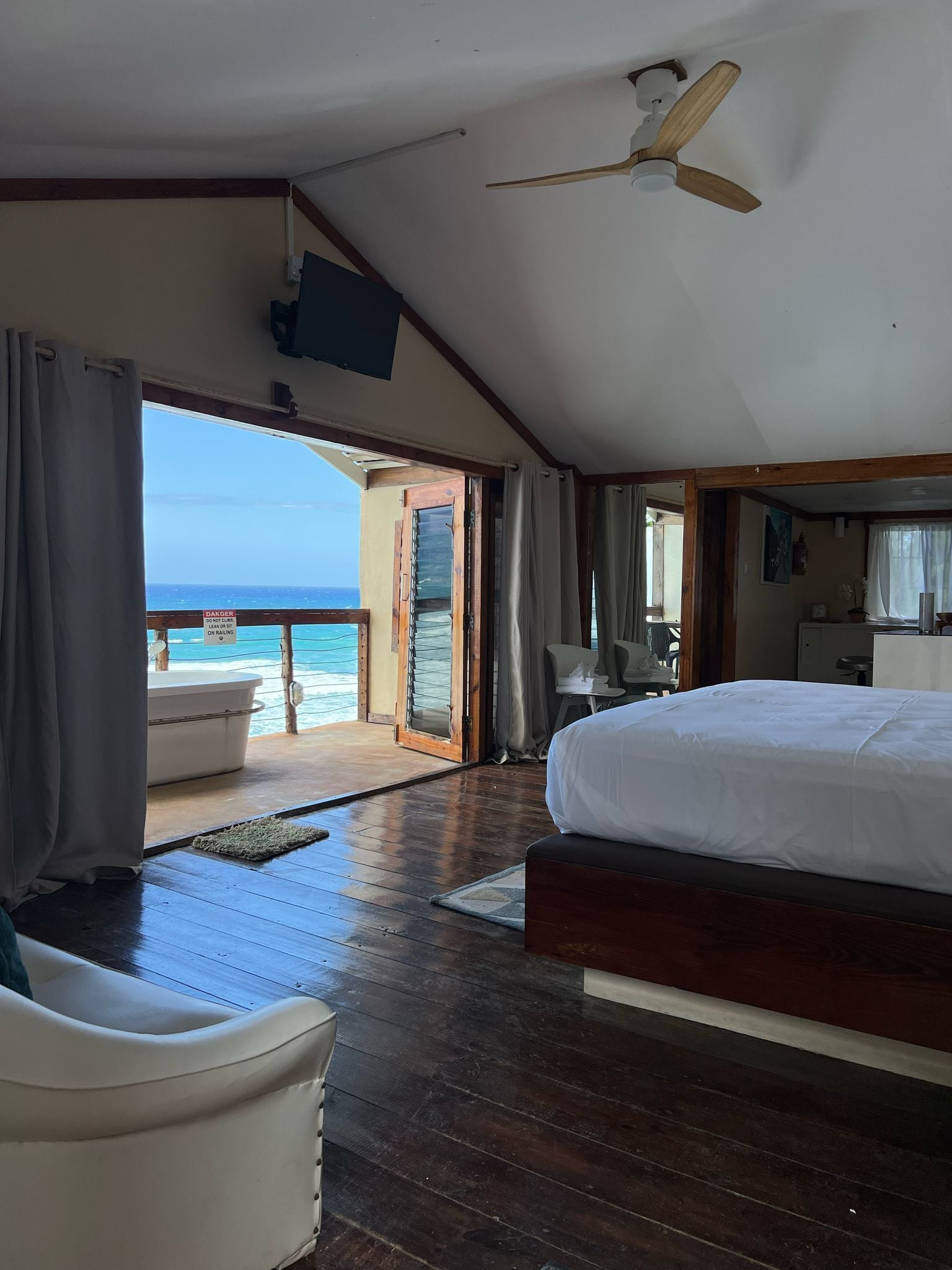 A room with a bed, a ceiling fan, a view of the ocean, and a door leading to an outdoor area.