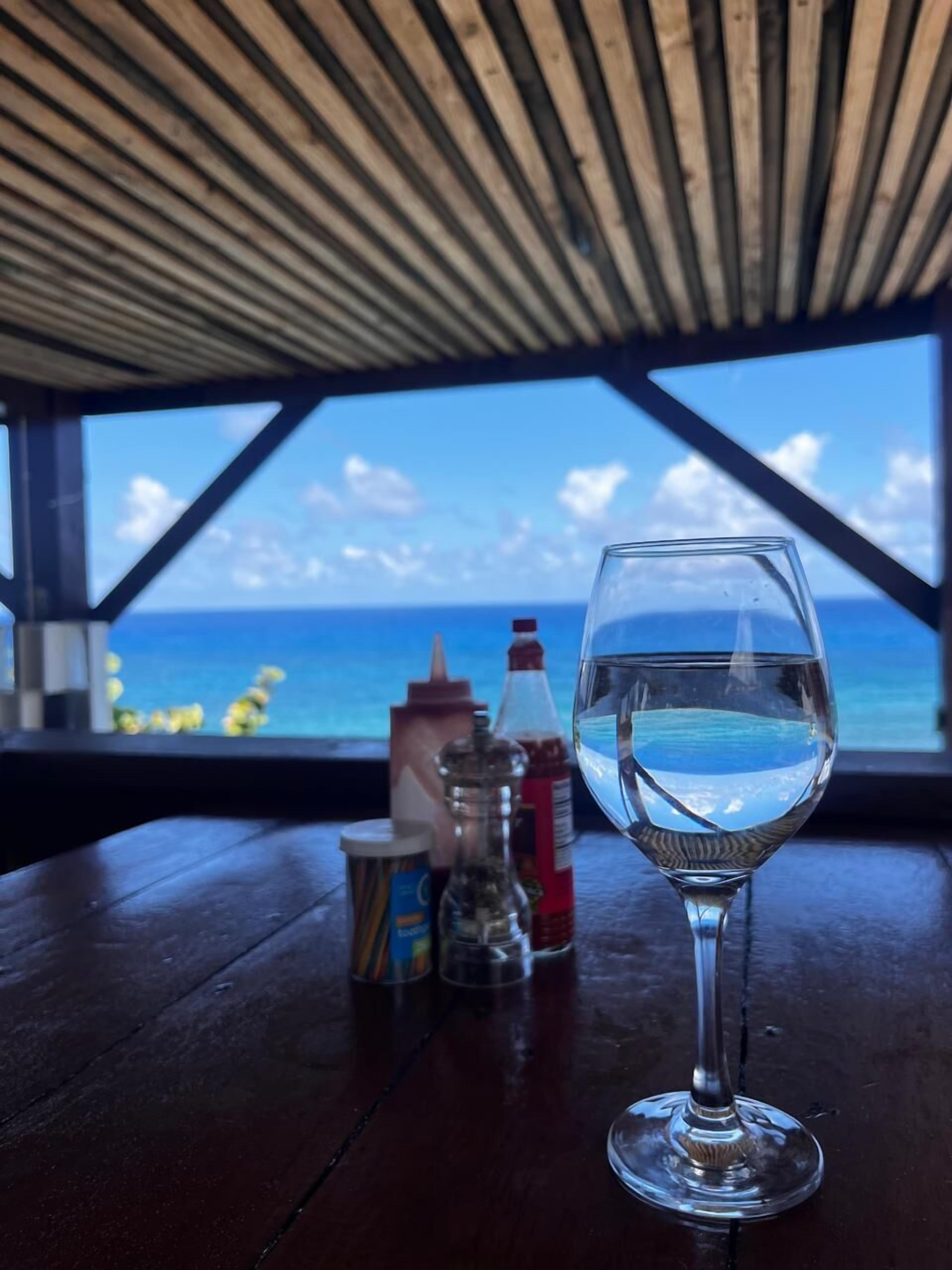 A table with a glass of water, condiments, and a view of the ocean.