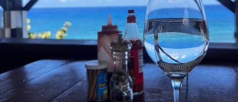 A table with a glass of water, condiments, and a view of the ocean.