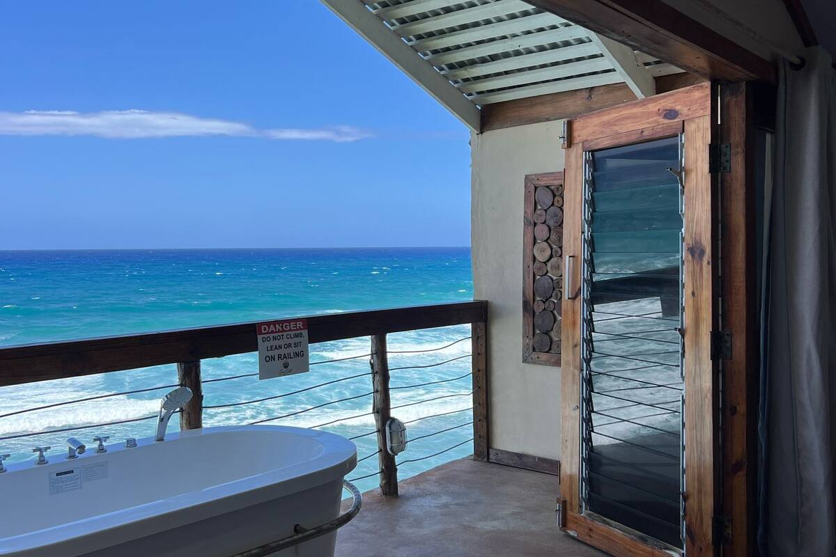 Un balcón con vistas al océano, una bañera y una puerta que da al interior.