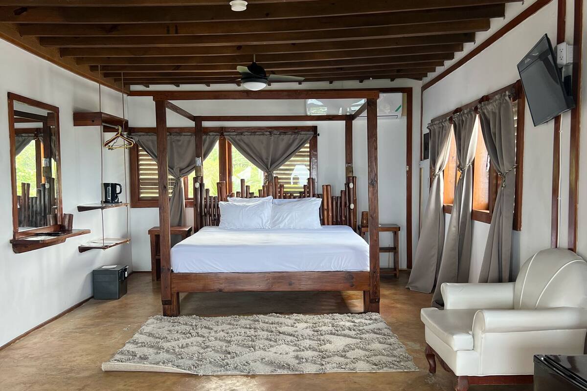 Un dormitorio con una cama con dosel de madera, un sofá blanco, un ventilador de techo y un televisor montado en la pared.