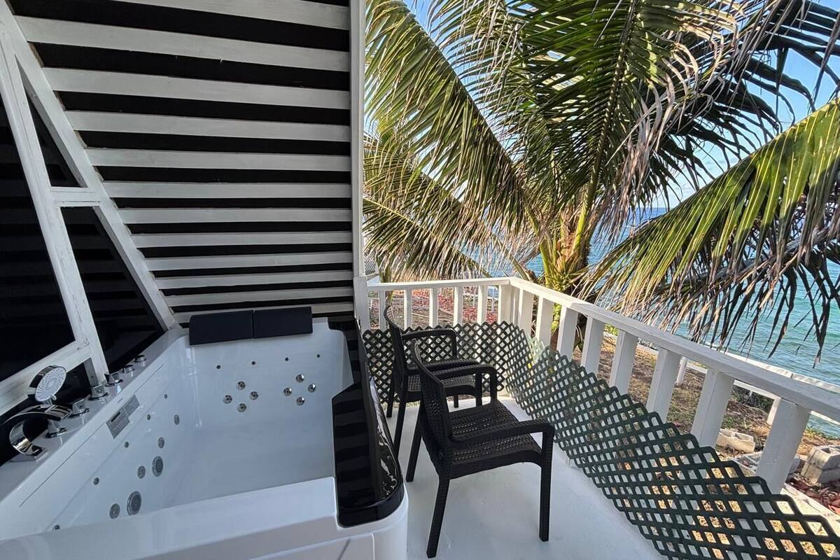 Un espacio de spa con hidromasaje y asientos, con vista a una playa con palmeras.