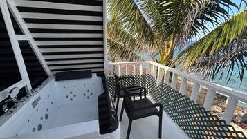 A spa area with a hot tub and seating, overlooking a beach with palm trees.