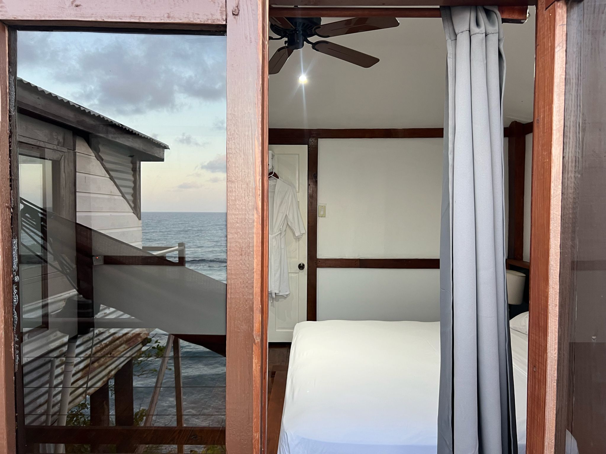 Una habitación con cama, ventilador de techo y vista al océano.