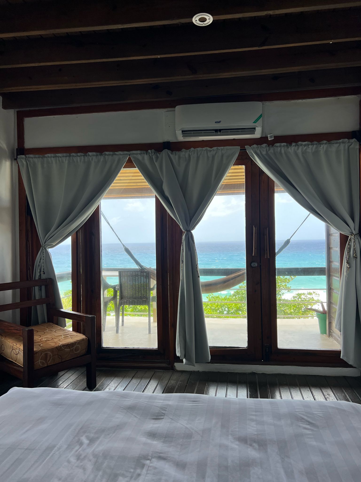 Une chambre avec un lit, une chaise et une vue sur l’océan, grâce à de grandes portes vitrées.