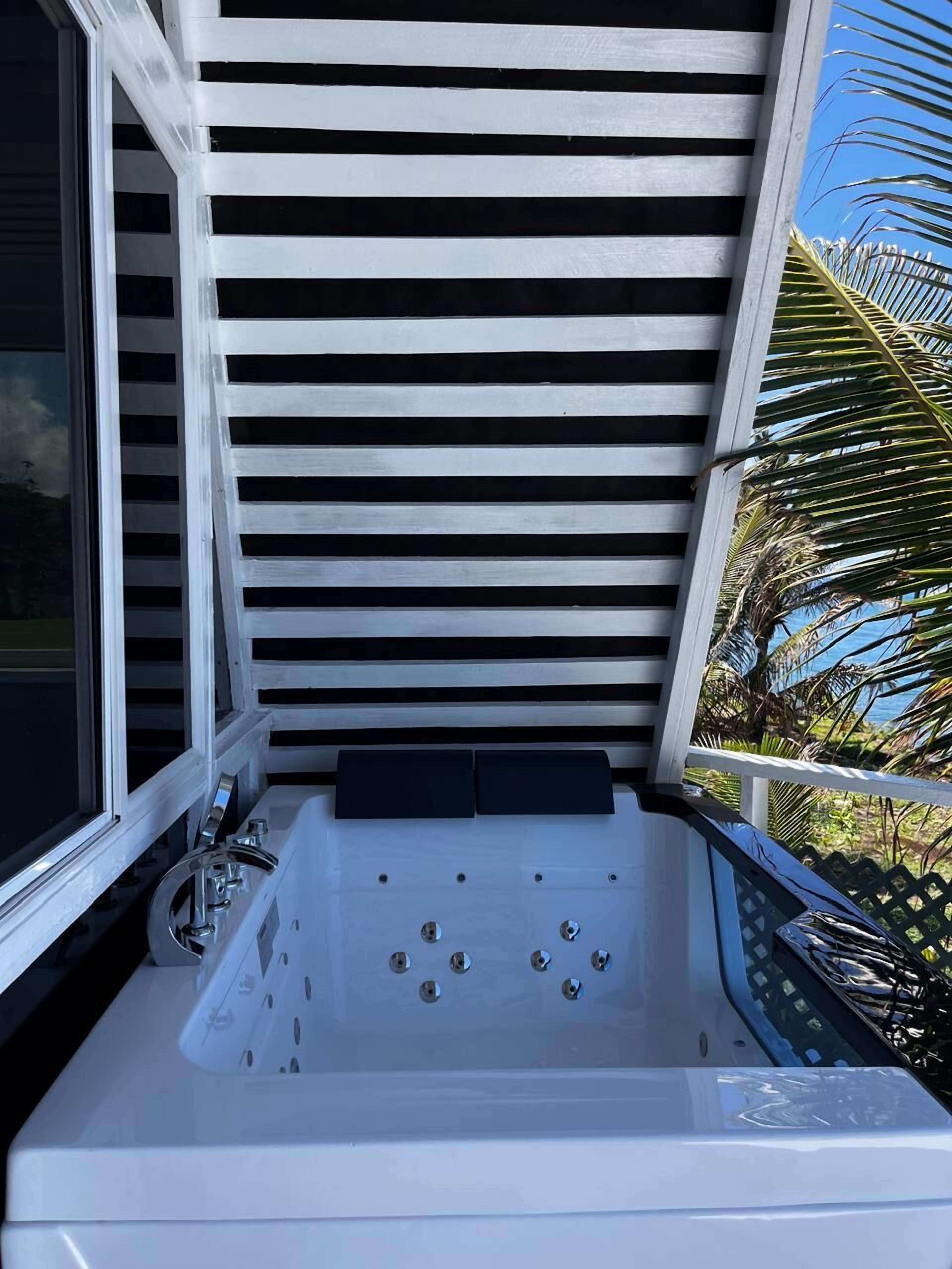 Esquina de una habitación con una bañera blanca, una ventana y vistas a palmeras.