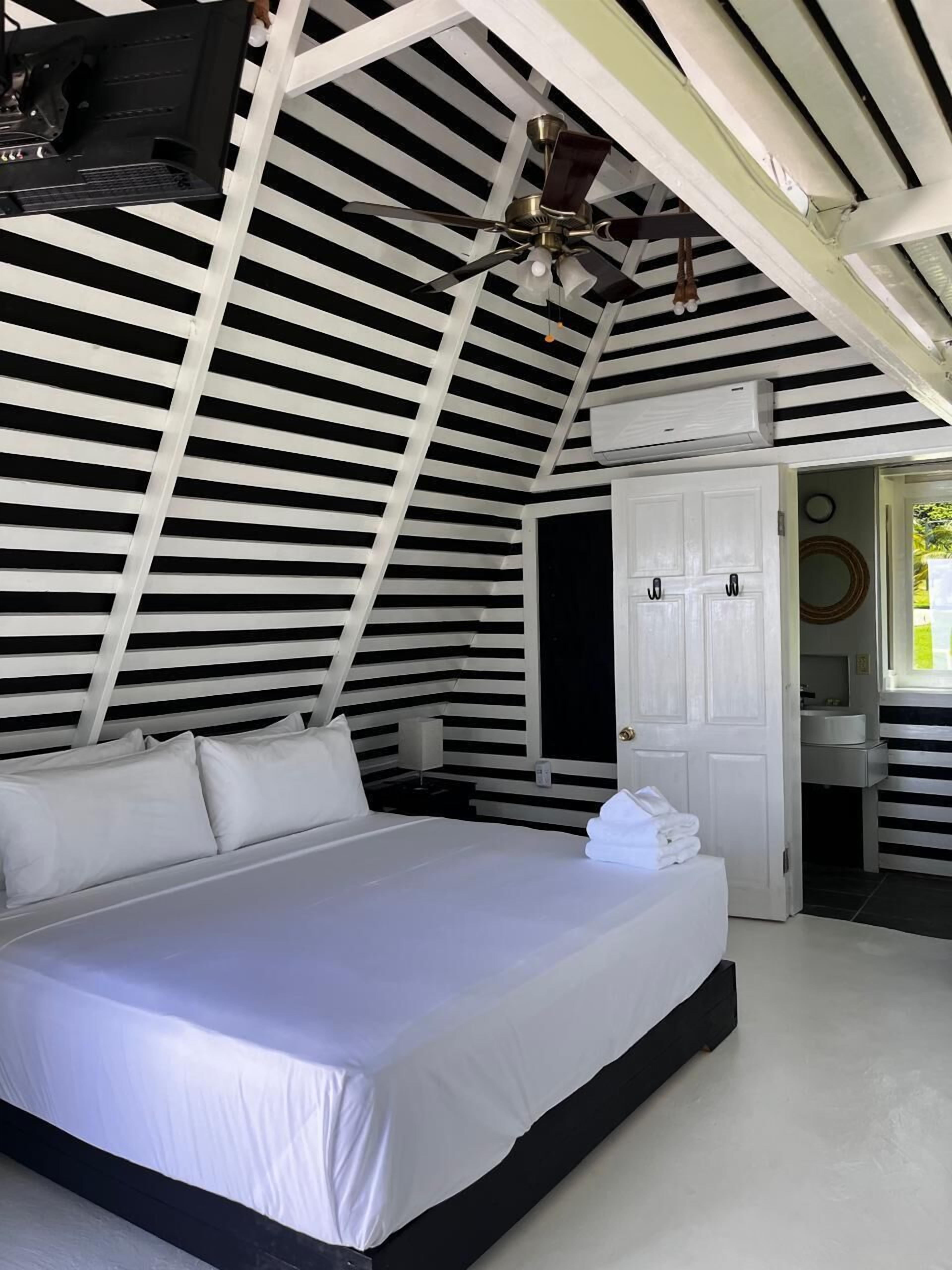 A bedroom with a bed, a ceiling fan, a door, and a bathroom visible through an open door.