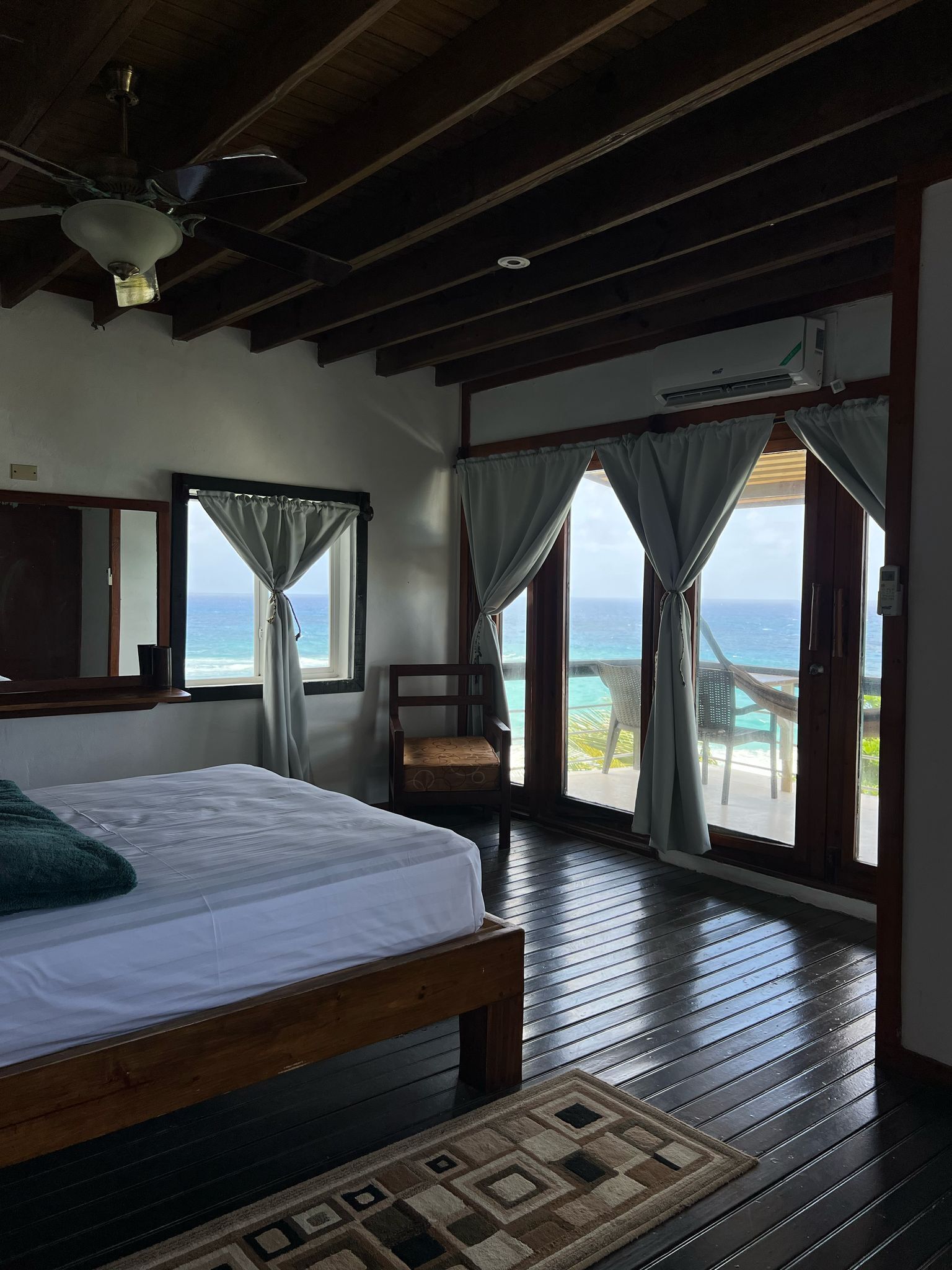 Quarto com cama, uma cadeira e vista para o mar através de amplas janelas.