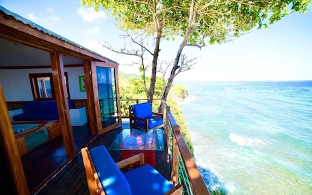 A wooden deck with blue chairs overlooking a clear blue sea.