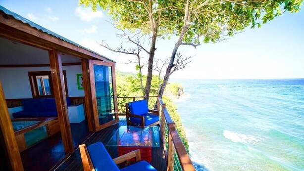 Una terraza de madera con sillas azules que da a un mar azul y despejado.
