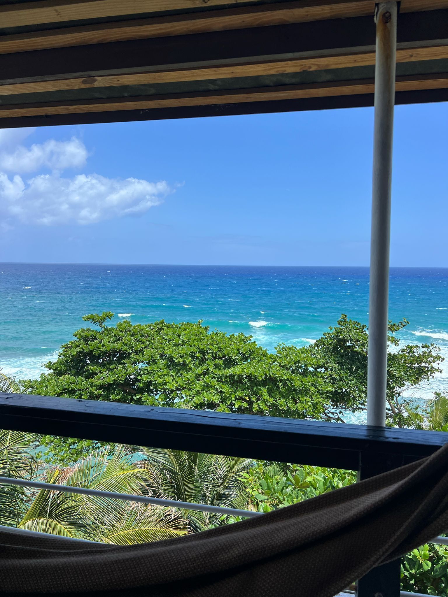 A view from a balcony with a wooden railing, overlooking a turquoise sea and a clear sky.