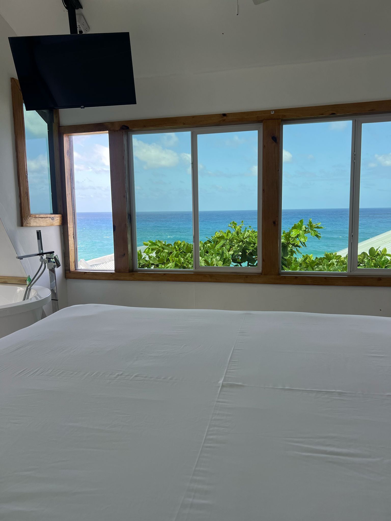 Un dormitorio con una cama grande, un televisor montado en la pared y vista al océano a través de amplias ventanas.