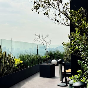 Une terrasse sur le toit offrant une vue sur les gratte-ciel de la ville, un mobilier d’extérieur moderne et une variété de plantes.
