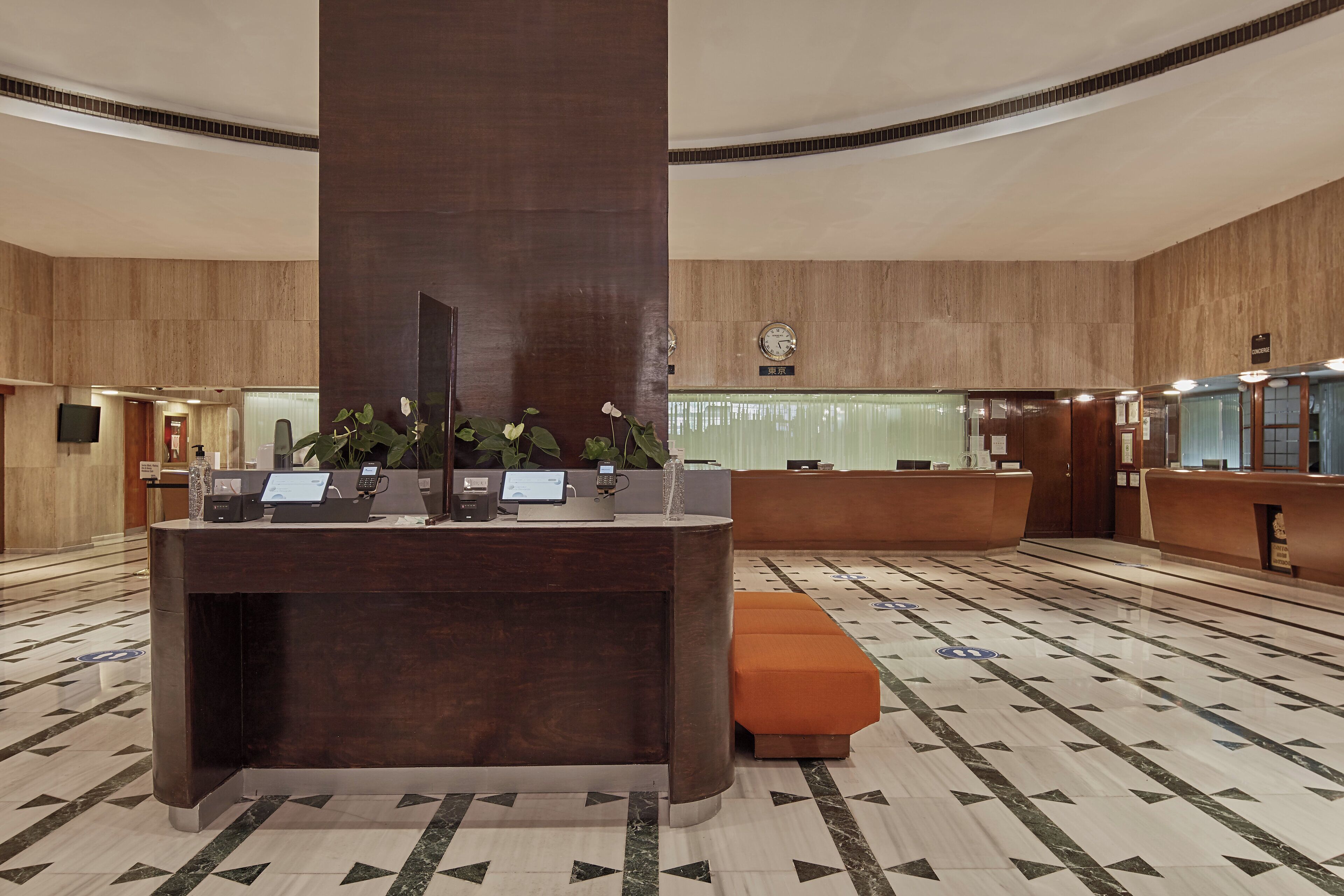 A hotel reception area with a marble floor, a central reception desk, and a clock on the wall.