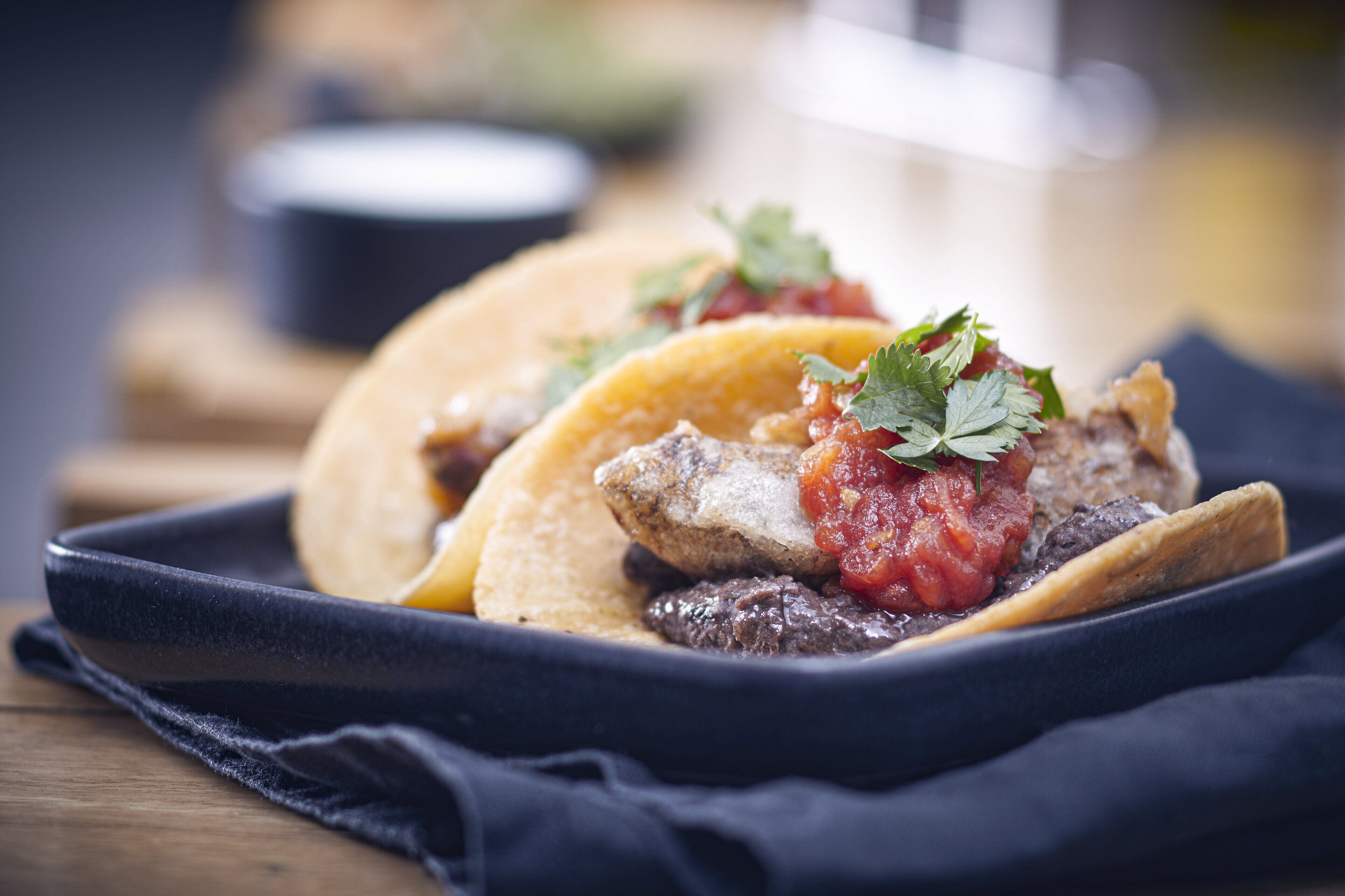 Una bandeja con dos tacos, uno con un guiso de carne visible y salsa roja, y el otro con aspecto similar.