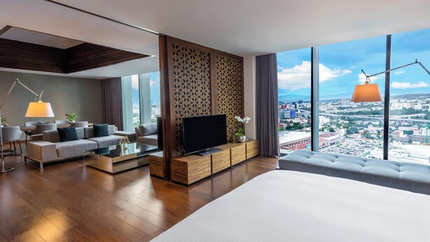 Una habitación de hotel moderna con una cama grande, un sofá, un televisor y vistas a la ciudad.