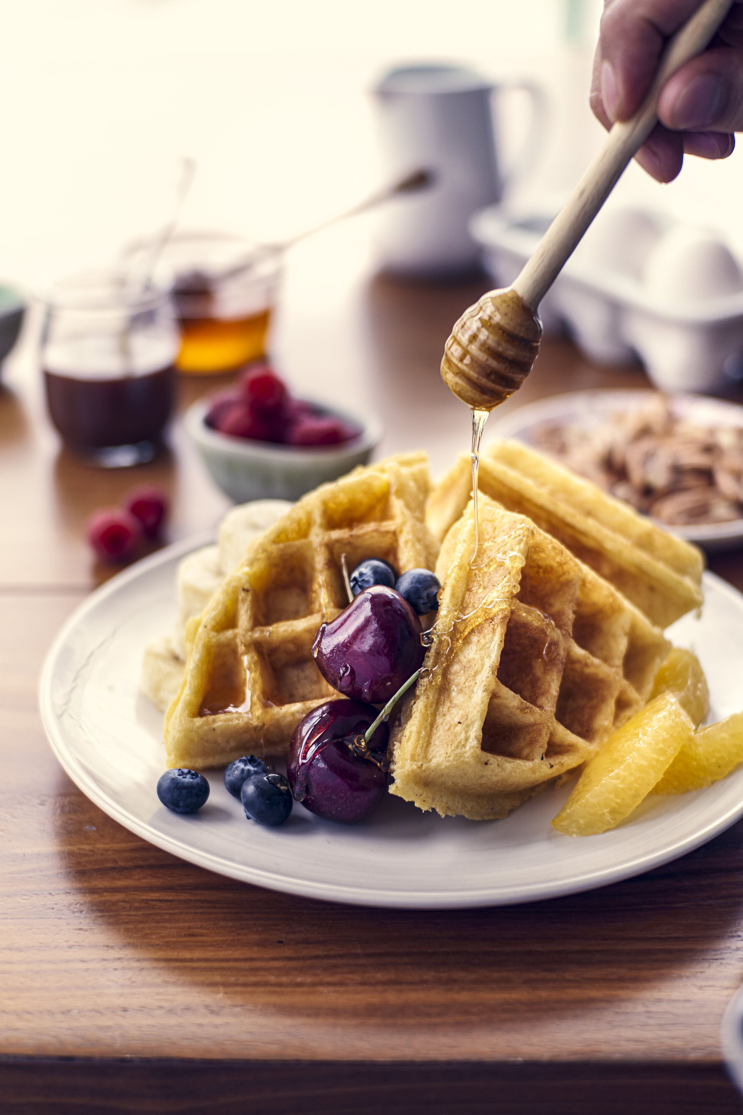 Une assiette de gaufres nappées de sirop et garnies de fruits, posée sur une table en bois.