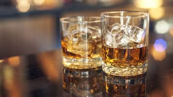 Two glasses of whiskey with ice cubes on a reflective surface.
