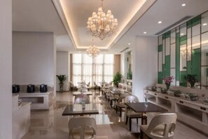 A modern hotel dining area with a chandelier, tables, chairs, and a long counter with a mirror and decorative items. - Vienna Classic Hotel(Dongguan Chang'an West Railway Station Modern City Store) (Dongguan)