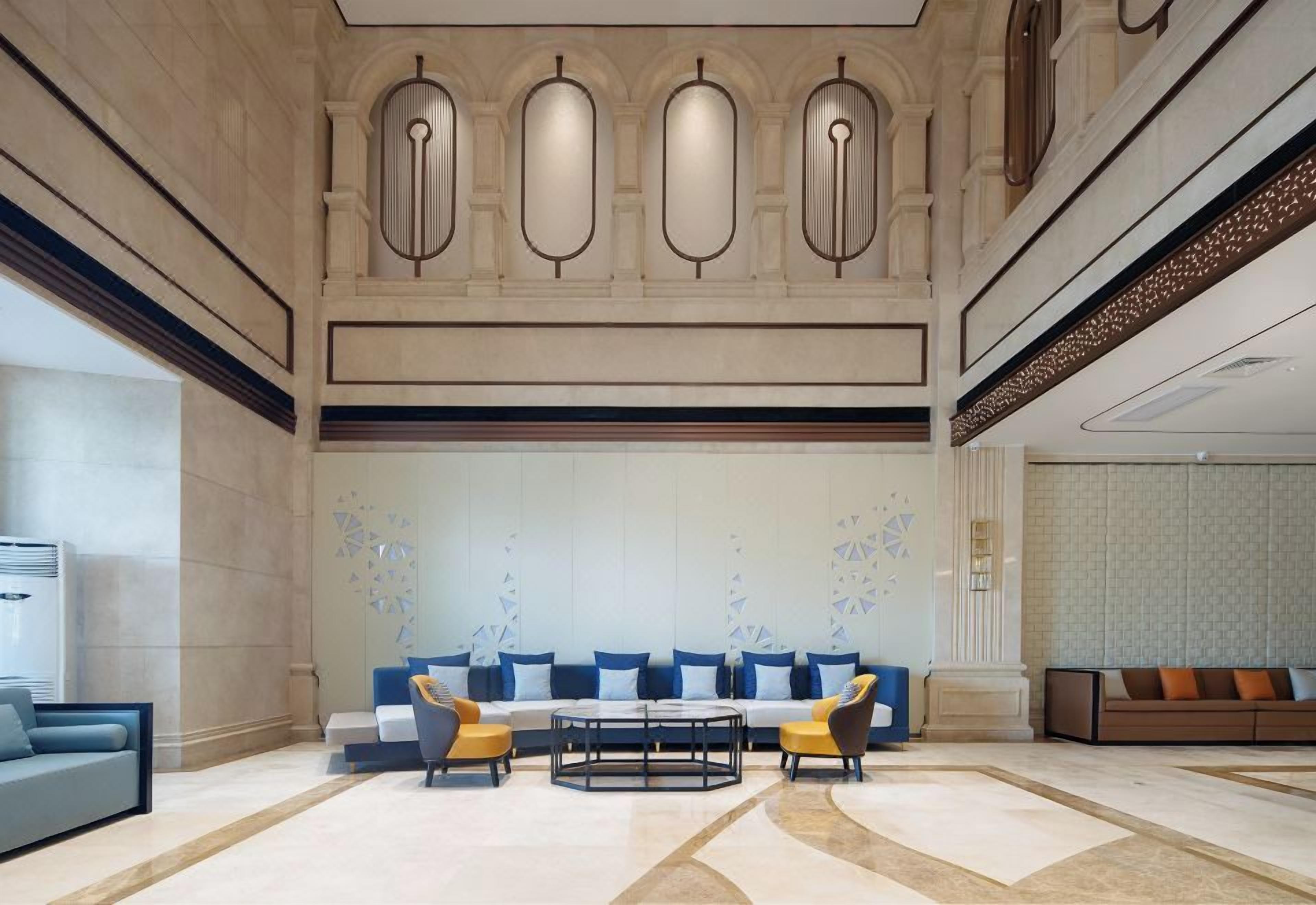 Un hall d’entrée spacieux avec un espace salon central, un comptoir d’accueil et un mur décoratif orné de motifs géométriques.
