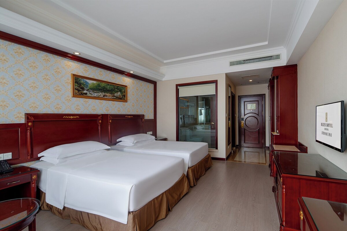 Habitación de hotel con dos camas, cabecera de madera, un cuadro en la pared y un escritorio con teléfono.