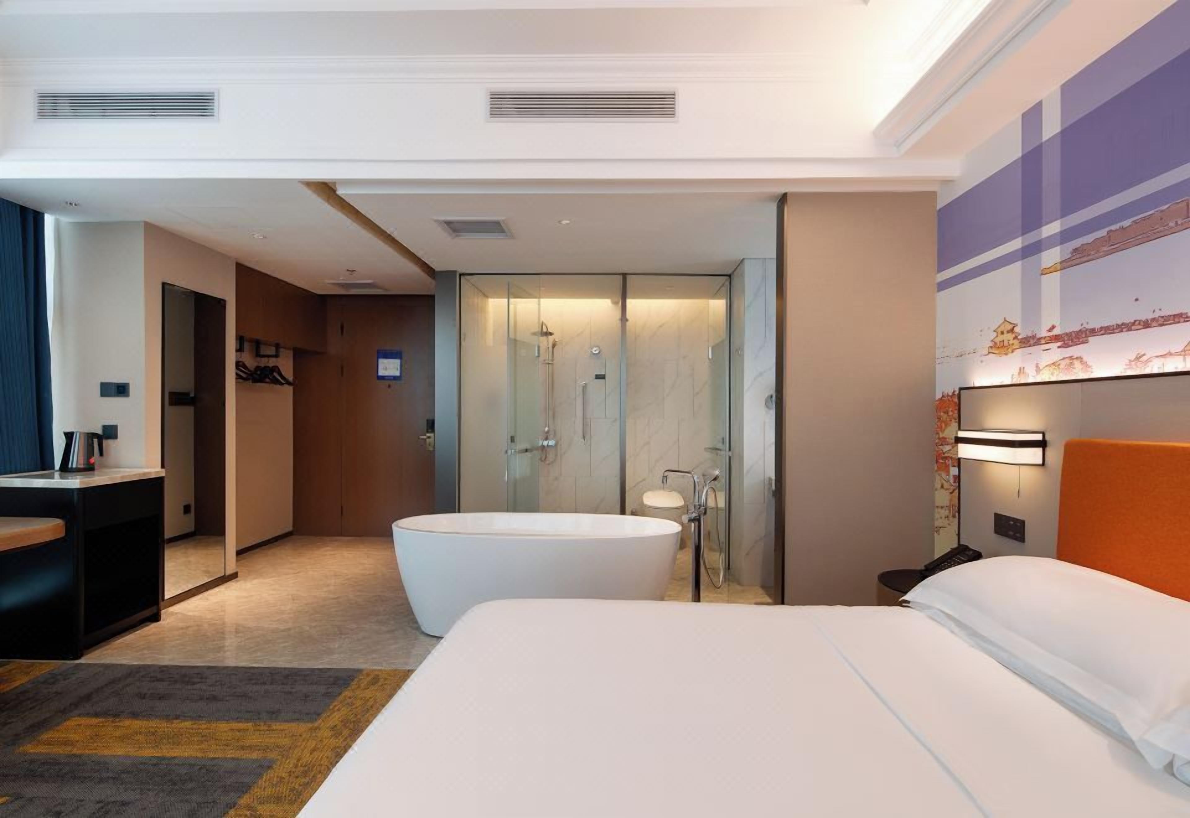 Une chambre d’hôtel moderne dotée d’un grand lit, d’une baignoire, d’un espace douche et d’un bureau avec une chaise.