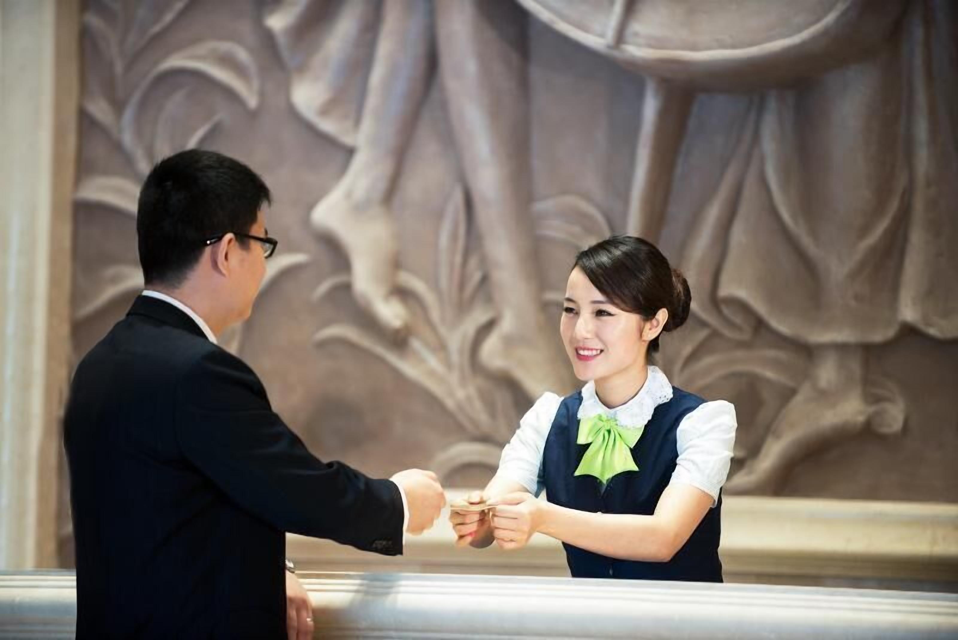 A man and a woman shaking hands in a formal setting with ornate wall carvings.