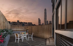 Une terrasse extérieure avec une table et des chaises, une clôture en bois et, en arrière-plan, la silhouette de la ville.