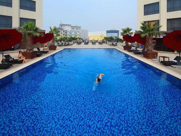 Une piscine où une personne nage, entourée de chaises longues et de parasols.