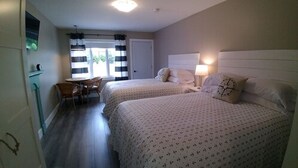 A hotel room with two beds, a small table, chairs, and a window with curtains.