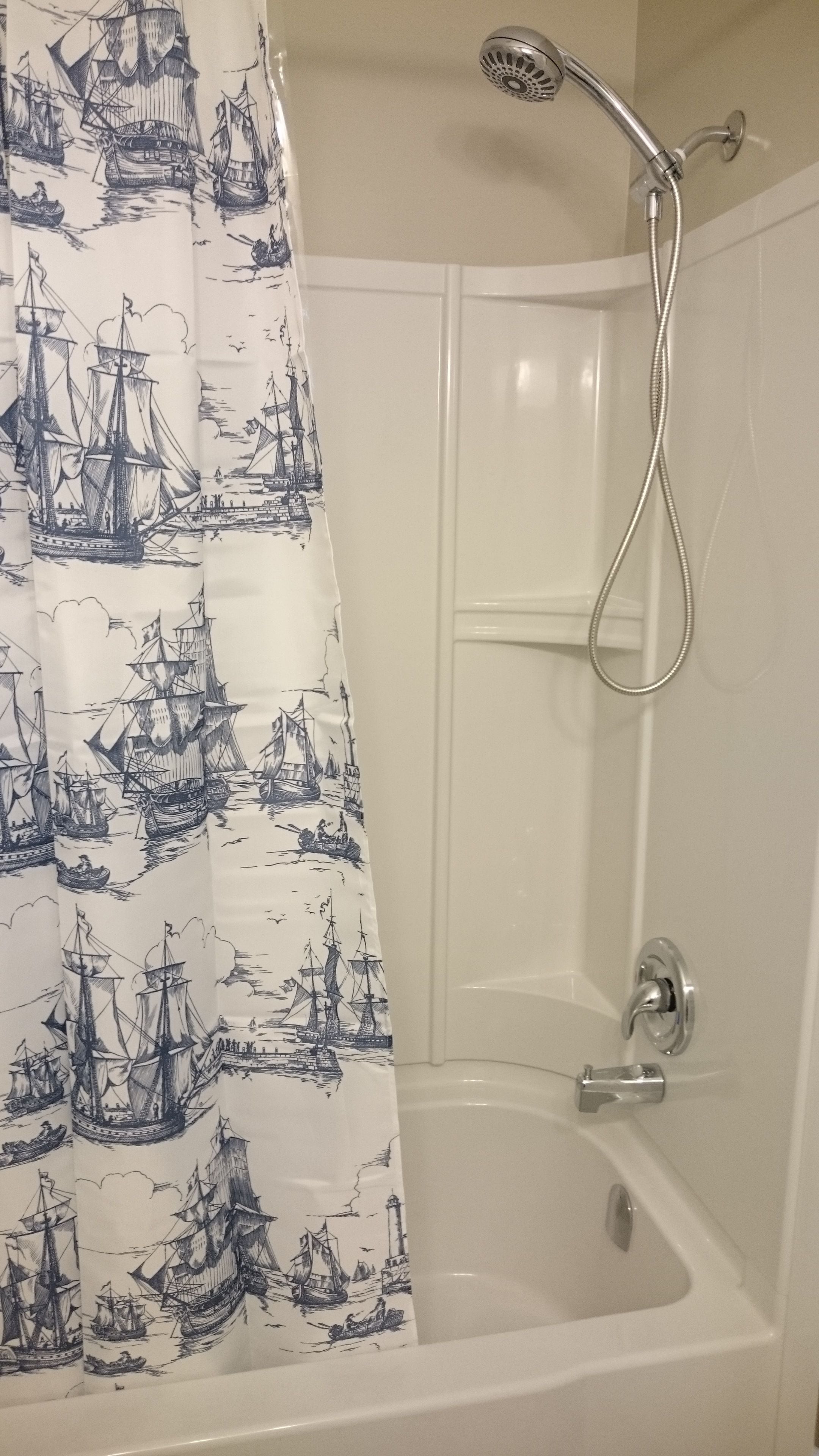 En dusch med ett draperi som har ett marint motiv, ett handhållet duschmunstycke och ett badkar.