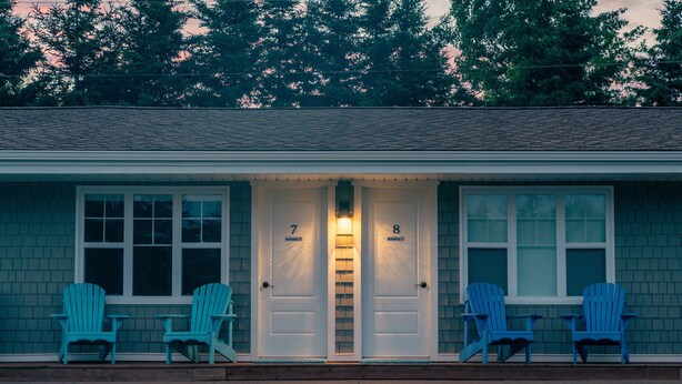 A two-story building with a porch, numbered doors, and four blue Adirondack chairs.