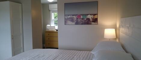 A bedroom with a bed, a dresser, a nightstand with a lamp, and a painting on the wall.
